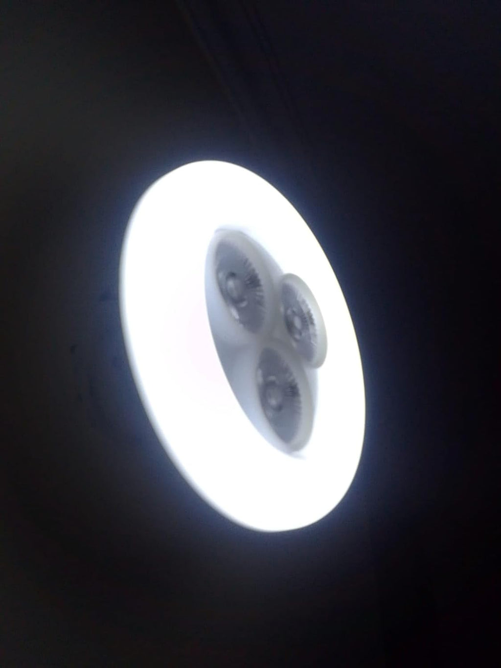 Circular light fixture emitting bright white light against a dark background

