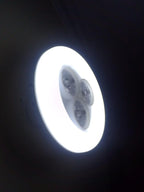 Circular light fixture emitting bright white light against a dark background

