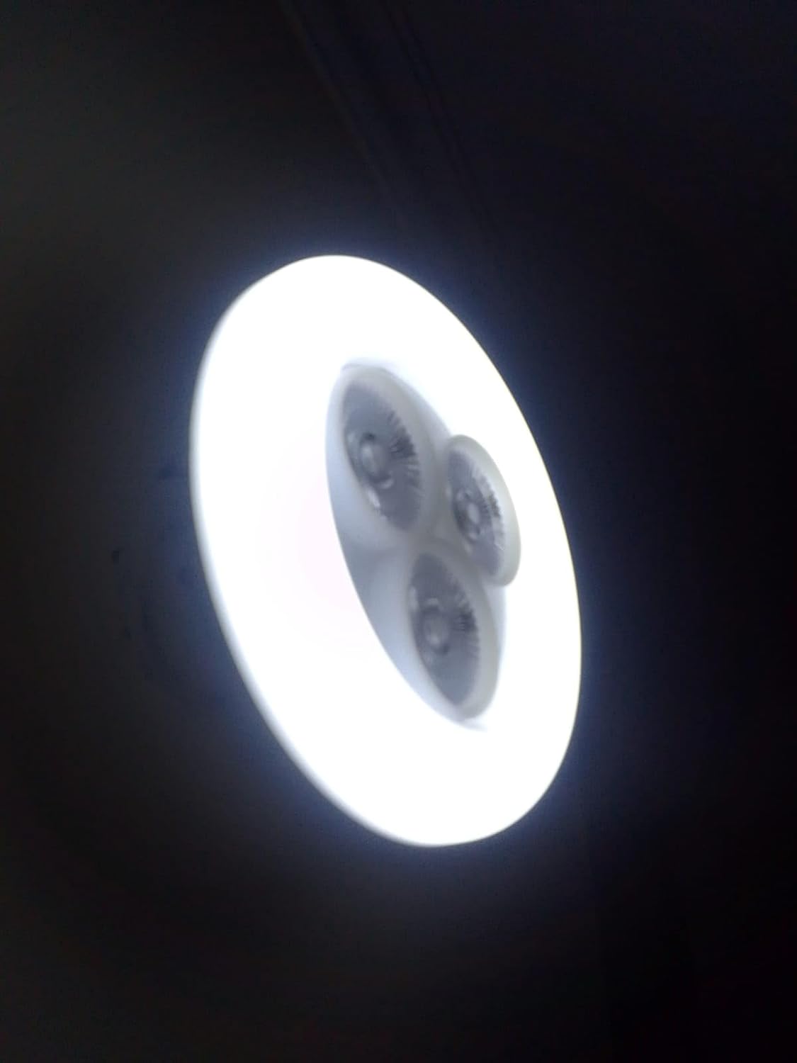 Circular light fixture emitting bright white light against a dark background

