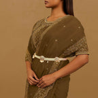 Woman wearing a brown saree with gold embroidery on a beige background

